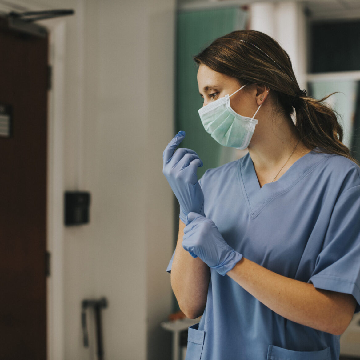 Female nurse with a mask putting on gloves