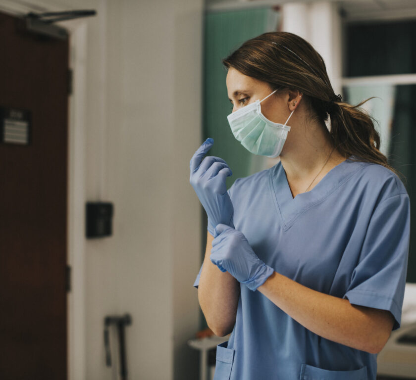 Female nurse with a mask putting on gloves